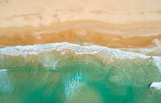 Aerial top view of turquoise ocean wave reaching the coastline.