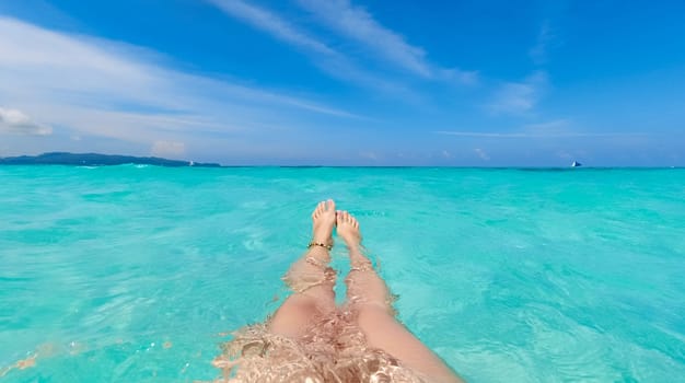 View of female's feet swimming under the crystal clear blue water in the sea on hot sunny day, underwater view.