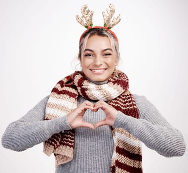 Christmas, woman and heart with smile in portrait for festive, winter and holiday on studio backdrop. Female person, cheerful and happy in celebration with shape for love in season for vacation.