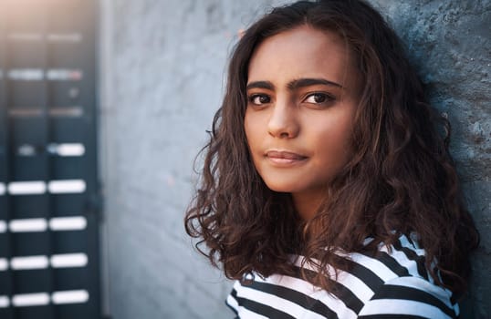 Young girl, portrait and face with fashion on a wall for casual clothing or outdoor style of gen z. Indian female person or model posing with curly hair and no expression for youth in confidence.