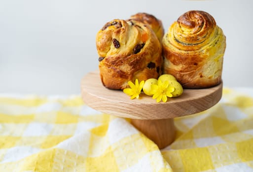 Freshly baked pastries are displayed on a wooden stand decorated with yellow flowers against a tartan background. Easter concept