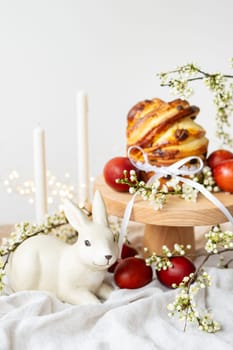 Festive table setting with ceramic bunny, red eggs, candles and Easter pastries, vertical photo. Easter holiday concept