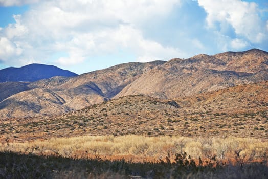 Landscape, sustainable and mountains in nature for agriculture, eco friendly and agro environment. Outdoor, travel and dry habitat with grass, blue sky and clouds for natural hiking trail by rocks