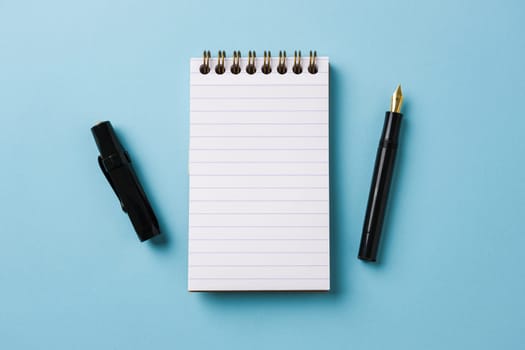 Top view of notebook and fountain pen on blue background