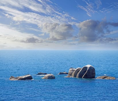 Clouds, blue sky and ocean with rock in nature for environment, sustainability and sunlight in ecosystem. Water, earth and wave by stone in California for clean air, sunshine and background of sea.