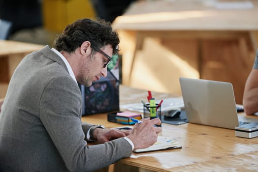 Businessman, notebook and brainstorming at desk for project, planning and teamwork in office. Mature male person, collaboration and research in workplace for start up company and global enterprise.