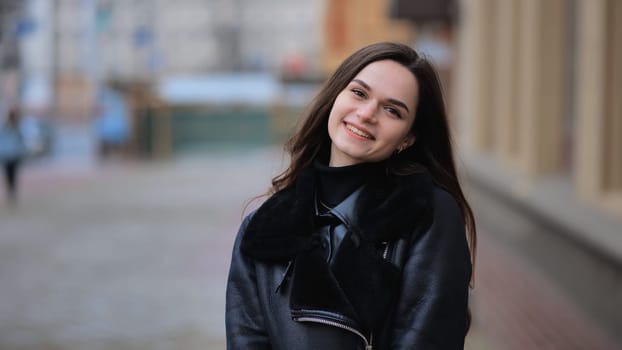 Happy brunette girl posing in black jacket in autumn in the city