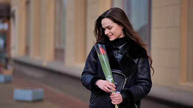 Portrait of a happy brunette girl with a tulip in the background of the city in the cold season