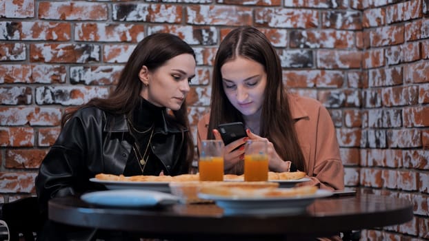 Two beautiful girls students have lunch in a city cafe and write a message on smartphones