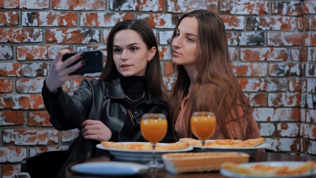 Two beautiful stylish young girls have lunch in a cafe and take a selfie on a smartphone