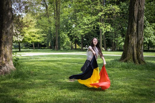 Portrait of one beautiful Caucasian little brunette girl in a skirt with flowing hair twirling with a Belgian flag in a city park on a summer day, close-up side view with copy space on the left.