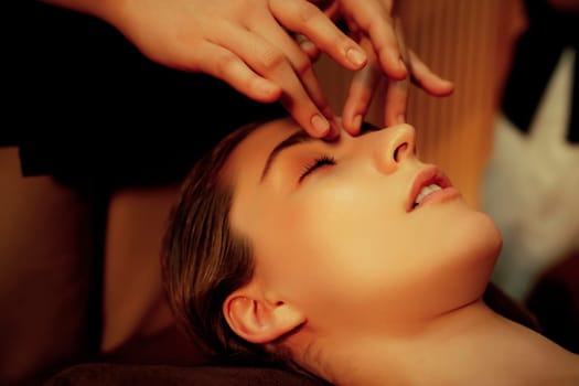 Caucasian woman enjoying relaxing anti-stress head massage and pampering facial beauty skin recreation leisure in warm candle lighting ambient salon spa in luxury resort or hotel. Quiescent