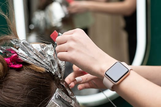 Beauty sphere. Hair coloring in a beauty salon. A master hairdresser-colorist dyes a client's brown hair blond. Apply lightening powder to hair and wrap hair in foil. Close-up. Business concept.
