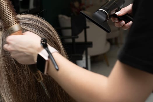 Beauty sphere. The master hairdresser does styling and combing the hair. Combs a client's long hair with a round brush and blow-dries it in a beauty salon. Close-up. Business concept. No faces.