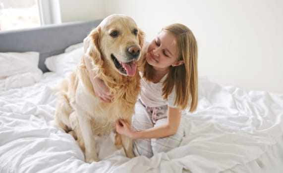 Sweet Little Girl Embracing A Lovely Golden Retriever Dog On A Bed In The Morning