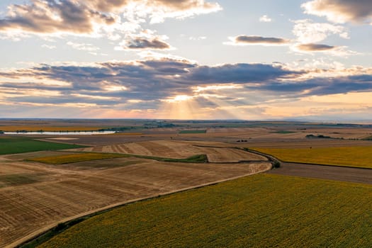 Stunning aerial view of road between autumn fields, and colorful sunset sky with rays