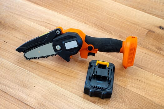 small accumulator chainsaw and battery on a wooden surface 