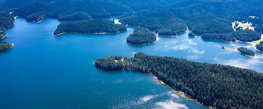 Panoramic aerial view of a lake,  blue water, and green forest.