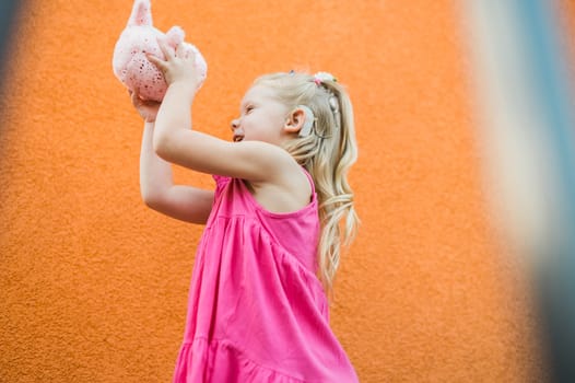 Child girl with hearing aids and cochlear implants having fun outdoor speak and playing. Copy space and empty place for advertising.