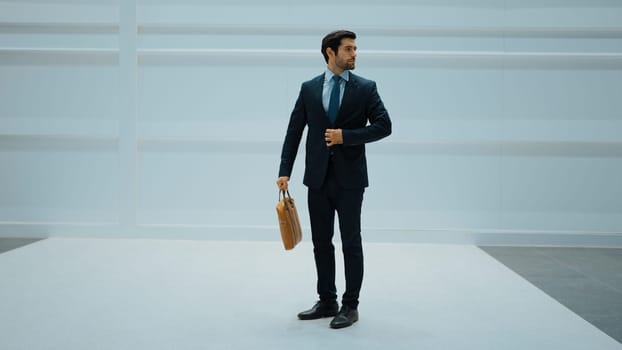 Professional business man standing with cool pose at white background. Manager holding bag while finding partner or looking around. Caucasian working man prepare himself for presentation. Exultant.