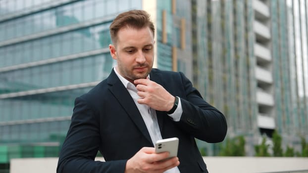 Skilled businessman using phone to chatting with team while standing roof top. Front view of project manager working on telephone with skyscraper view while communicate with marketing team. Urbane.