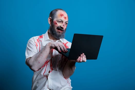 Mindless worker worked to death doing mind numbing tasks on laptop. Man working like zombie, inputting data on notebook, doing monotonous work, isolated over studio background