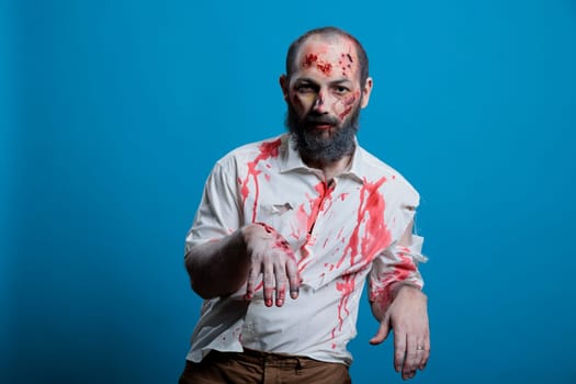 Man dressed as spooky zombie for Halloween event looking ferocious and frightening. Person costumed as undead demon covered in blood and scars looking dangerous, studio background