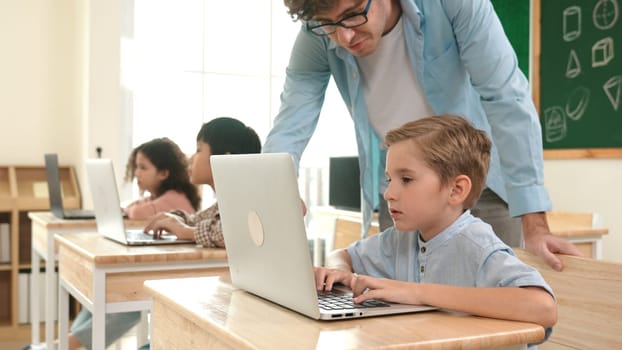 Caucasian teacher helping energetic boy coding engineering prompt while diverse student using software generated AI. Children sitting and programing system. Cute student learning about code. Pedagogy.