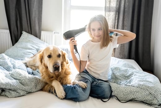 Happy Little Girl Drying Hair With A Hairdryer, Sitting With Dog On A Bed