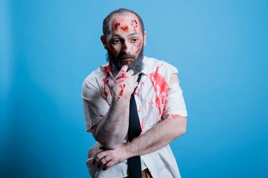 Actor dressed as horror movie brainless zombie repeating lines between scenes on set. Man costumed as mindless infected creature preparing for role, isolated over studio background