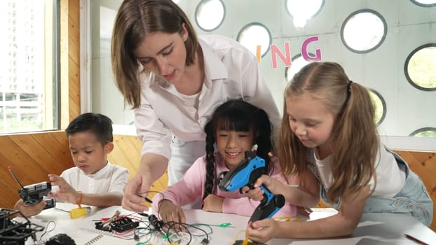 Teacher looking at children while diverse student looking at screen. Children excited in presentation while drawing or writing art books at table with toys and color pencil placed on table. Erudition.