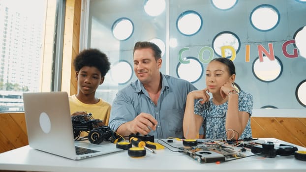 Caucasian student asking teacher about code and pointing at laptop screen. Professional instructor answer girl question while boy repair car model at table with electronic tool placed. Edification.