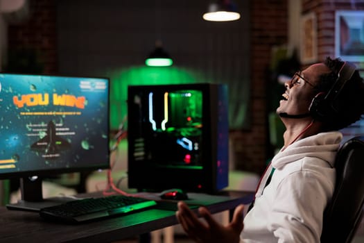 Excited gamer celebrating winning online multiplayer futuristic videogame match. African american man enjoying leisure time at home, feeling ecstatic about gaming championship victory