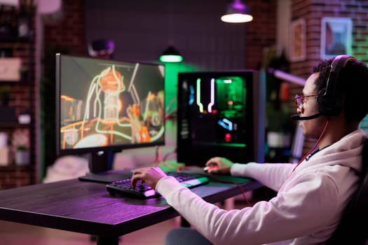 Man in brick wall living room playing video games on gaming PC at computer desk, enjoying day off from work. Gamer battling enemies in online multiplayer shooter from neon lights ornate home
