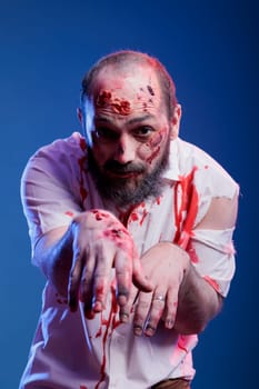 Portrait of man dressed as terrifying creepy zombie covered in blood for halloween party. Person wearing scary makeup, pretending to be undead monster with scars, studio background