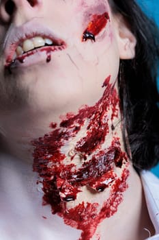 Extreme close up shot of bloody injury on woman neck acting as zombie for horror film scene. Gore undead corpse scars with fake blood achieved through professional SFX makeup for Halloween costume