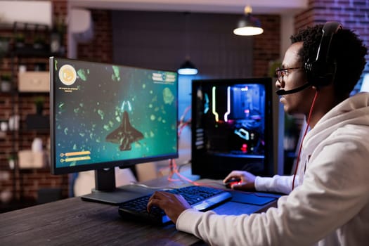 Gamer playing classic arcade action videogame, flying through space debris. African american man enjoying leisure time at home using high tech gaming PC to solve missions in singleplayer game