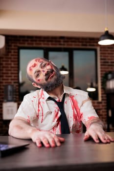 Weary man sunken on desk chair, feeling like being worked to death, making grimaces. Lifeless businessman covered in bruises and turned into zombie, concept of capitalism pressure