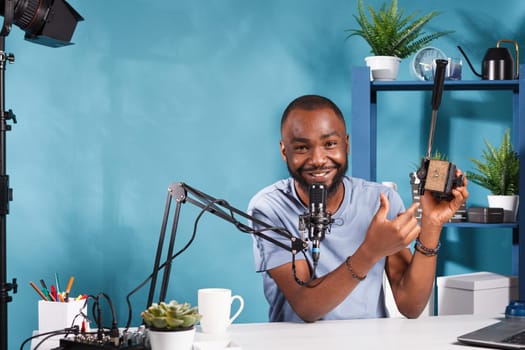 Vlogger examining tripod fluid head while recording review and product presentation video. Smiling man showing camera stabilization device videography equipment while live streaming