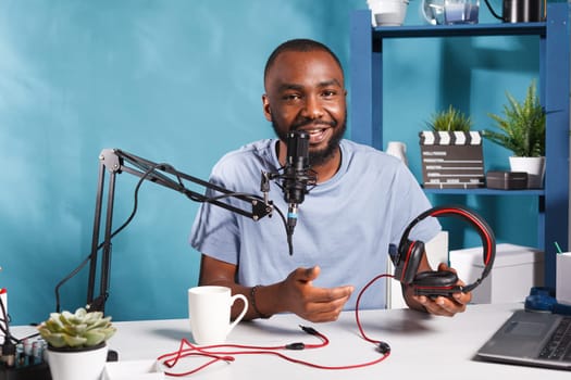 Smiling internet influencer promoting headphones while recording video and looking at camera. Cheerful african american vlogger reviewing device, speaking in microphone and broadcasting live