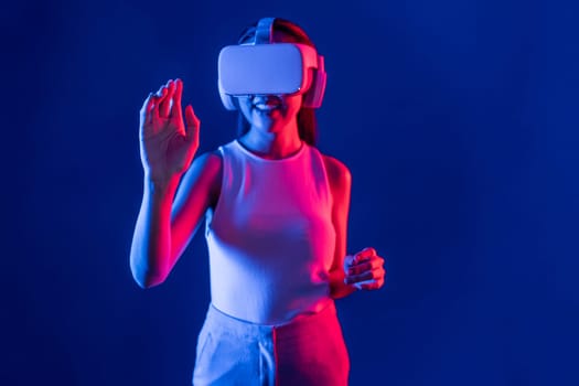 Smart female standing with surrounded by cyberpunk neon light wear VR headset connecting metaverse, futuristic cyberspace community technology. Woman using hand touching virtual object. Hallucination.