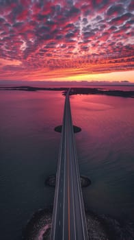 Aerial view of a long bridge over calm waters at sunset with dramatic cloud formations