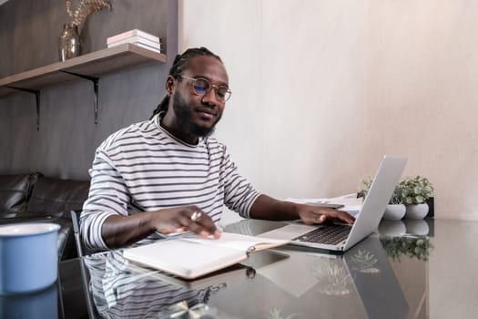 Young African American businessman spends his weekend working from home using his laptop in the living room..