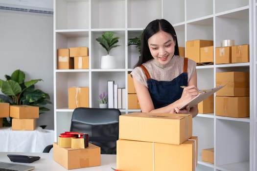 A small SME business owner receives product orders and writes shipping information on cardboard boxes in the home office to prepare for delivery..