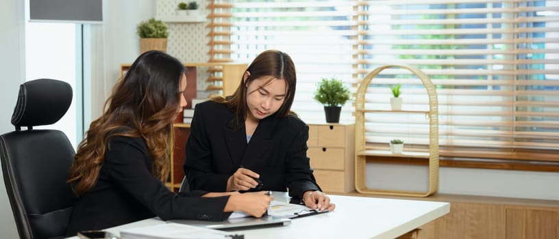 Professional businesswomen discussing financial accounting papers at co working space.