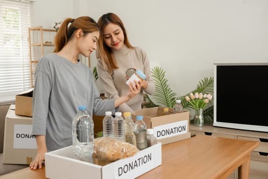 Two young female volunteers help pack food into donation boxes and prepare to donate them to charity..