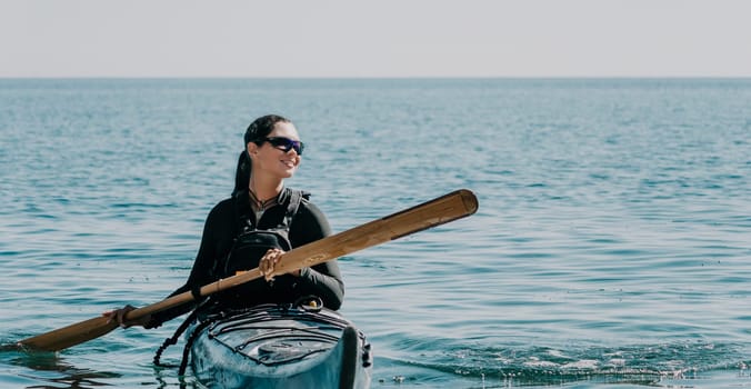 Happy smiling woman in kayak on ocean, paddling with wooden oar. Calm sea water and horizon in background