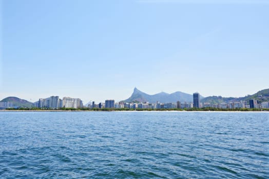 Water, ocean and city with nature, blue sky and vacation with getaway trip, Rio de Janeiro and adventure. Beach, aerial view and outdoor with mountains, sunshine and summer with holiday and travel.