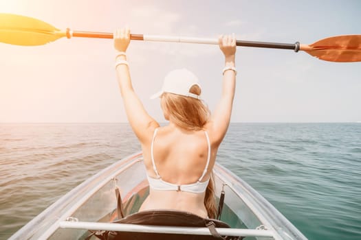 Woman in kayak back view. Happy young woman with long hair floating in transparent kayak on the crystal clear sea. Summer holiday vacation and cheerful female people having fun on the boat.