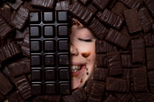 The face of a caucasian woman surrounded by sweets. The girl is smeared in chocolate